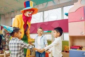 Funny clown with cheerful children play counting game together. Birthday party celebrating in playroom, baby holiday in playground. Childhood happiness
