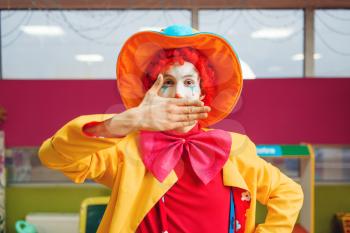 Funny clown shows tricks with facial expressions in children's area. Birthday party in playroom, baby holiday in playground. Childhood happiness, childish leisure, entertainment with animator