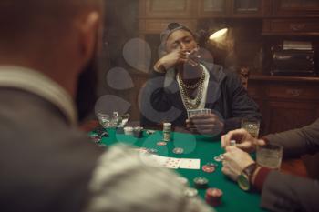 Three poker players sitting at gaming table with green cloth in casino. Games of chance addiction, gambling house. Men leisures with whiskey and cigars,