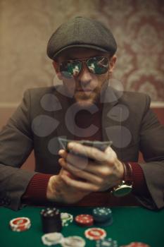 Serious poker player in sunglasses playing in casino. Games of chance addiction. Man with cards in hands leisures in gambling house