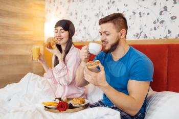 Romantic love couple, breakfast in bed at home, good morning, caring husband. Harmonious relationship in young family. Man and woman resting together in their house, carefree weekend