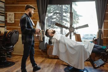 Barber in hat and bearded customer, beard cutting. Professional barbershop is a trendy occupation. Male hairdresser and client in hair salon