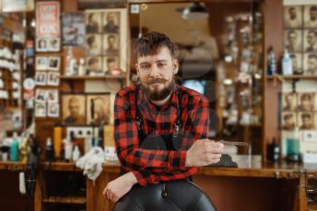 Barber with razor blade poses at the chair. Professional barbershop is a trendy occupation. Male hairdresser in retro style hair salon, accessories for cutting