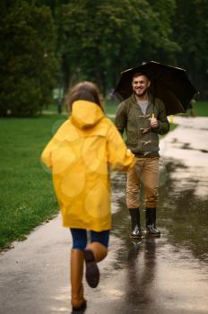Happy love couple dating in park, summer rainy day. Man and woman under umbrella in rain, romantic date on walking path, wet weather in alley