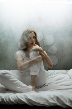 Crazy woman with pillow sitting in bed, dark room on background. Psychedelic person having problems every night, depression and stress, sadness, psychiatry hospital