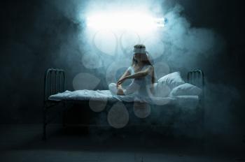 Blindfolded psycho woman sitting in bed, dark room on background. Psychedelic female person having problems every night, depression and stress, sadness, psychiatry hospital