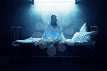 Mad woman in garlands sitting in bed, insomnia, dark room on background. Psychedelic female person having problems every night, depression and stress, sadness
