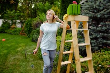 Happy woman looks on flower bed in the garden. Female gardener takes care of plants outdoor, gardening hobby, florist lifestyle and leisure