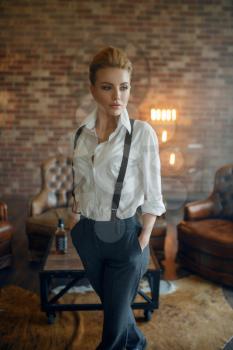 Woman in strict clothes poses in studio, retro fashion, gangster style. Vintage business lady in office with brick walls