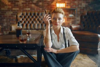 Business woman in strict clothes relax on the floor with whiskey and cigar, retro fashion, gangster style, female macho. Vintage lady in office with brick walls