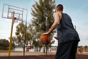 Basketball player prepares to make a throw on outdoor court. Male athlete in sportswear holds ball on streetball training