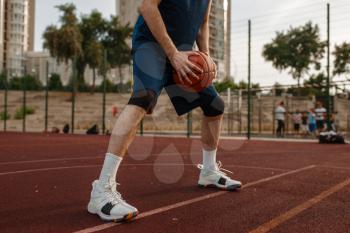 Male basketball player holds a ball on outdoor court. Male athlete in sportswear on streetball training, summer stadium