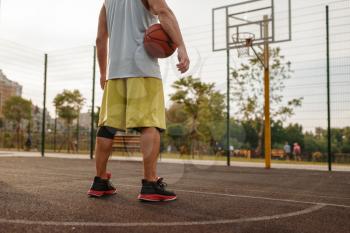 Male basketball player with ball standing at the basket on outdoor court, back view. Male athlete in sportswear on streetball training, summer stadium