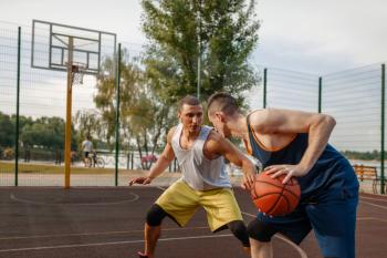 Two basketball players playing intense match on outdoor court. Male athletes in sportswear play the game on streetball training