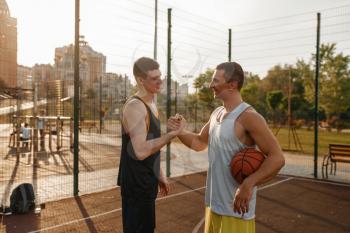 Two basketball players shake hands after playing on outdoor court. Male athletes in sportswear after streetball training, sport friendship