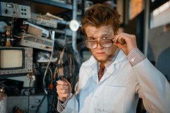 Strange engineer holds electric tube in laboratory. Electrical testing tools on background. Lab equipment, engineering workshop