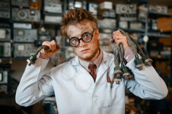 Strange scientist with electric terminal connected to his ear, dangerous test in laboratory. Electrical testing tools on background. Lab equipment, engineering workshop