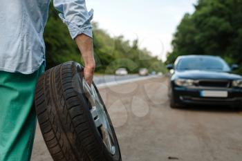 Car breakdown, man puts the spare tyre. Broken automobile or problem with vehicle, trouble with punctured auto tire on highway