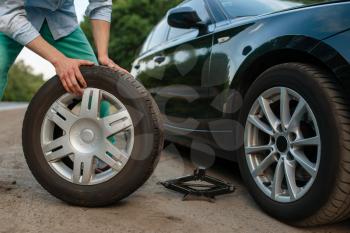 Car breakdown, man puts the spare tire. Broken automobile or problem with vehicle, trouble with punctured auto tyre on highway