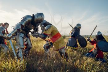 Medieval knights in armor and helmets fight with sword and axe, great battle. Armored ancient warrior in armour posing in the field