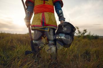 Medieval knight in armor holds axe and helmet, great tournament. Armored ancient warriors in armour posing in the field