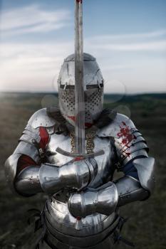 Medieval knight in armor and helmet poses with sword, great battle. Armored ancient warrior in armour posing in the field