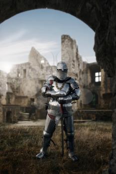 Medieval knight in armor and helmet poses in castle, great battle. Armored ancient warrior in armour posing in the field