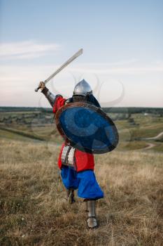 Medieval knight with sword poses in armour, great fighter. Armored ancient warriors in armor posing in the field