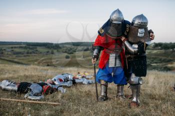 Wounded medieval knights in armor looks at the dead after great battle. Armored ancient warrior in armour posing in the field