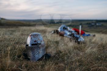 Helmet in blood, dead medieval knight on background, great tournament. Armored ancient warrior in armour posing in the field