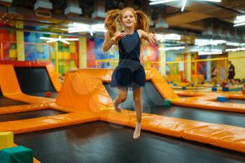 Adorable little girl bouncing on kids trampoline, playground in entertainment center. Play area indoors, playroom
