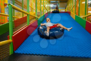 Little boy rides on tubing, playground in entertainment center. Play area indoors, playroom