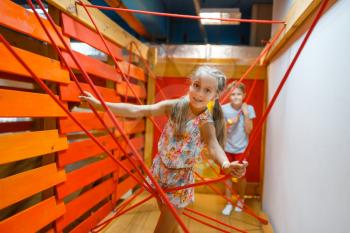Two little girls playing in rope labyrinth, playground in entertainment center. Play area indoors, playroom