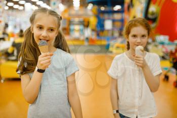 Two girls eats ice cream in the entertainment center. Children leisures on holidays, childhood happiness, happy kids on playground