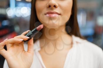 Woman holds lipstick at her face in cosmetics store. Buyer in luxury beauty shop salon, female customer in fashion market