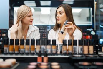 Cosmetician and woman choosing nail varnish at the showcase in cosmetics store. Luxury beauty shop salon, female customer and beautician in fashion market