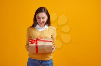 Happy woman holding gift box with red ribbons, yellow background. Pretty female person got a surprise, event or birthday celebration