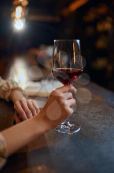 Woman with glass of red wine sitting at the counter in bar. One female person in pub, human emotions, leisure activities, nightlife