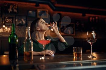 Stressed woman drinks different alcohol at the counter in bar. One female person in pub, human emotions, leisure activities, nightlife