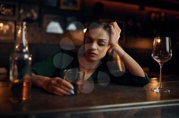 Stressed woman drinks alcohol beverage at the counter in bar. One female person in pub, human emotions, leisure activities, nightlife