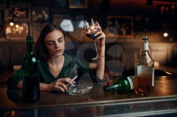Unhappy woman drinks alcohol beverage at the counter in bar. One female person in pub, human emotions, leisure activities, depression