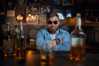 Serious man in sunglasses sitting at the counter in bar. One male person resting in pub, human emotions, leisure activities, nightlife