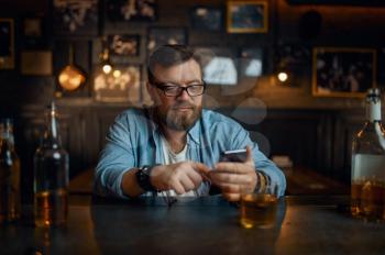 Man with mobile phone sitting at the counter in bar. One male person resting in pub, human emotions, leisure activities, nightlife