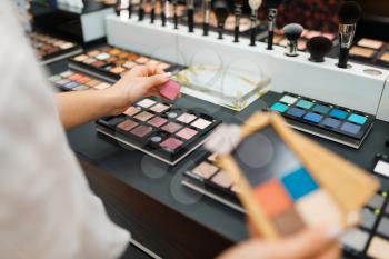 Woman holds eyeshadows at the shelf in cosmetics store. Buyer at the showcase in luxury beauty shop salon, female customer in fashion store