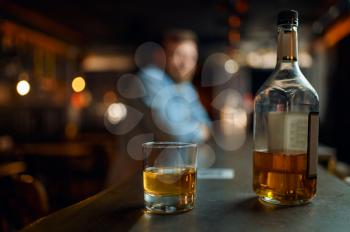 Bottle of alcohol and glass on counter in bar, male person on dlur background. Man resting in pub, human emotions and leisure activities, stress relief concept