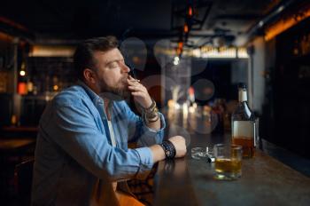 Stressed bearded man drinks alcohol at the counter in bar. One male person resting in pub, human emotions and leisure activities, depression, stress relief