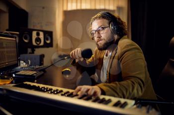 Sound engineer in headphones holds microphone, recording studio interior on background. Synthesizer and audio mixer, musician workplace