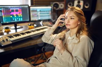 Female dj in headphones listening record, recording studio interior on background. Synthesizer and audio mixer, musician workplace, creative process