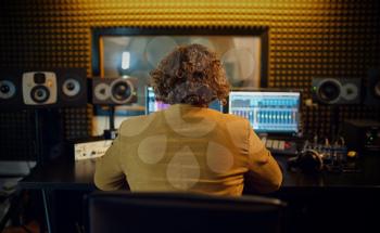 Male sound engineer at mixing consol, back view, recording studio interior on background. Synthesizer and audio mixer, musician workplace, creative process