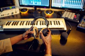 Male sound engineer holds headphones at mixing consol, recording studio interior on background. Synthesizer and audio mixer, musician workplace, creative process